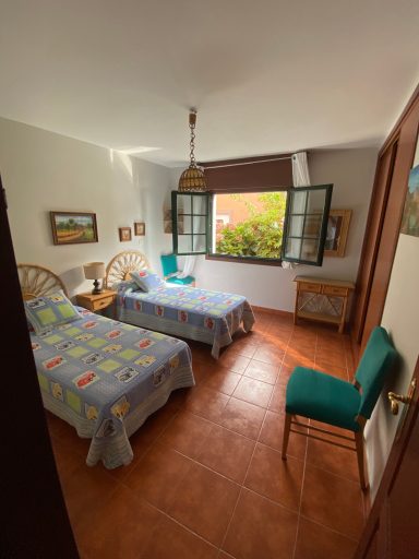 Habitación 4 Habitación con dos camas individuales, ventana abierta y una silla verde. Decoración sencilla.