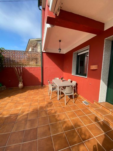 Zona exterior delantera Terraza con mesas y sillas, paredes rojas, y piso de baldosas en un día soleado.