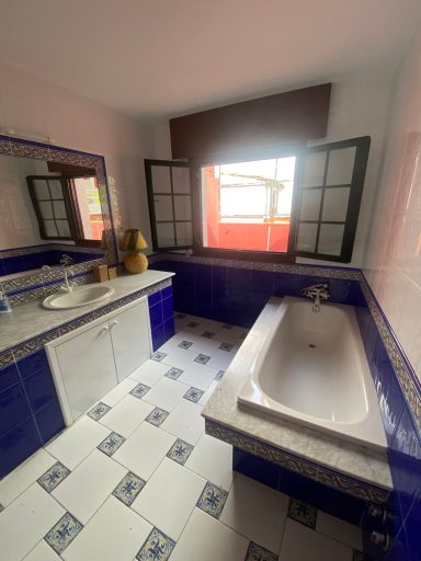 Baño de servicio planta alta Baño con azulejos azules, lavabo, bañera y ventana con luz natural.