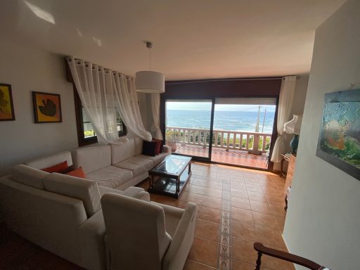Salón planta alta Salón luminoso con sofá, mesa de café y vista al mar desde la ventana.